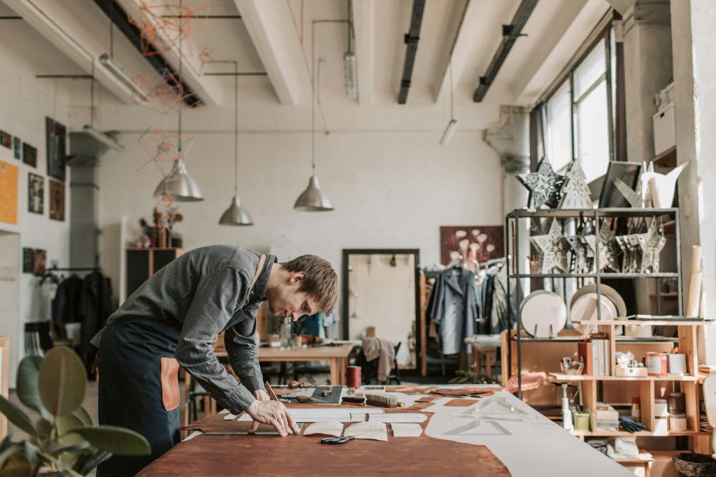 A man diligently crafting leather goods in a bright, organized workshop, emphasizing traditional craftsmanship.